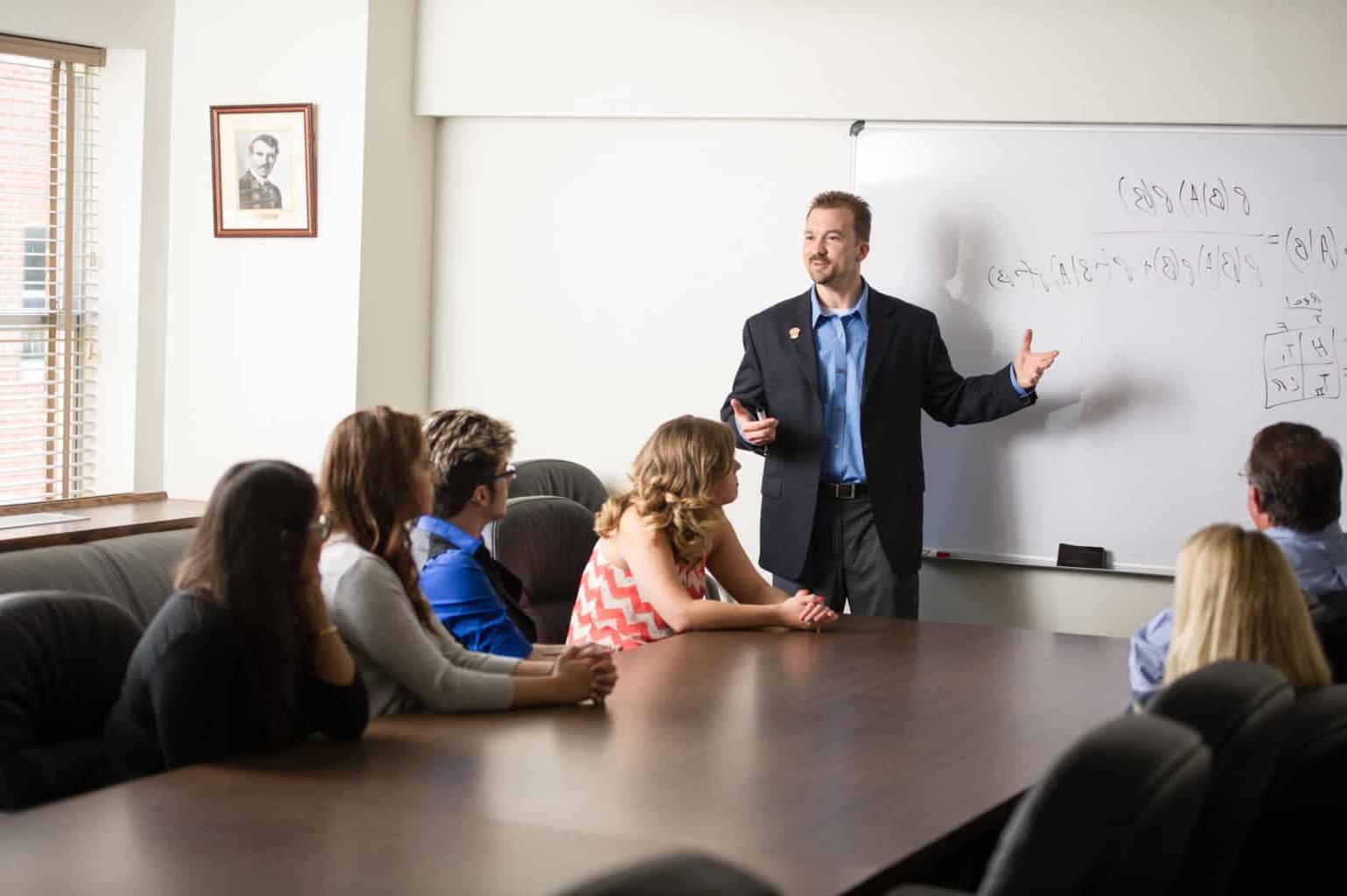 Psychology instructor teaching class around a large boardroom table.
