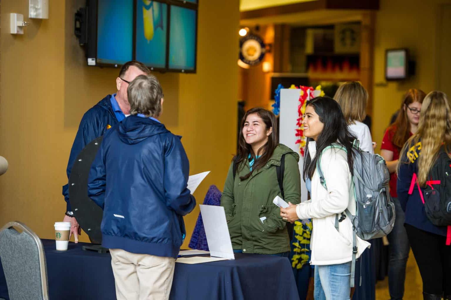 Two students talking with two professors during a student organizations fair on campus.